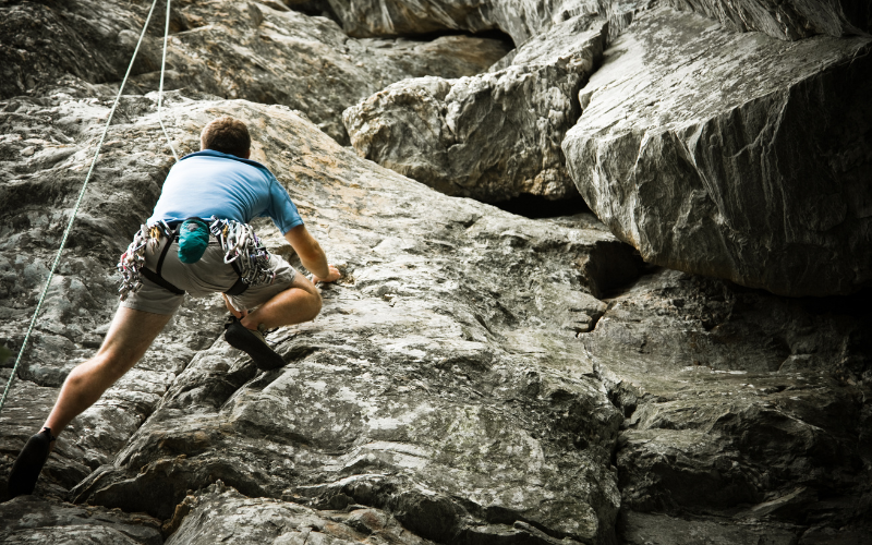 Climber ascending red sandstone cliffs at Badami rock climbing site in Karnataka